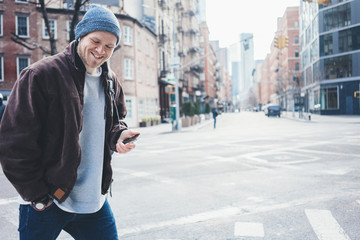 Smiling man with mobile phone on the crossroad walking in the city