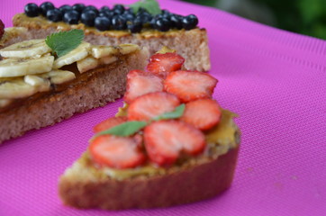 different delicious toasts on green or pink crimson background. Healthy sandwich for breakfast or snack. Toast with raspberries, strawberries, banana and blueberries and peanut butter. picnic concept