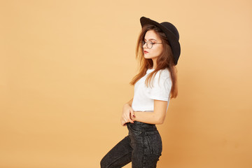 Pretty brunette girl with long hair in the black hat on her head dressed in white t-shirt and black...