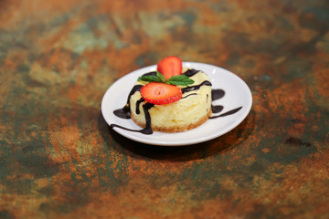 Cheesecake with strawberry and dark chocolate on a white plate with rustic background dessert