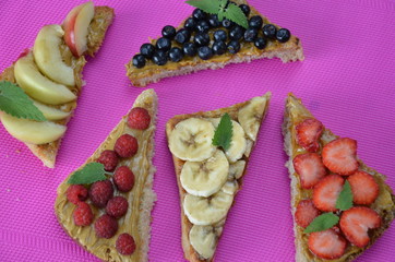 different delicious toasts on green or pink crimson background. Healthy sandwich for breakfast or snack. Toast with raspberries, strawberries, banana and blueberries and peanut butter. picnic concept