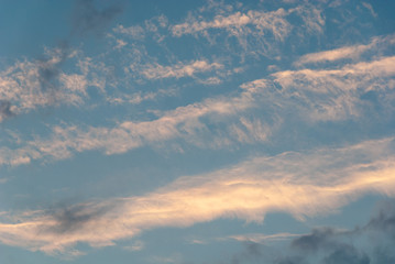 Light clouds high up in sky lit up by the setting sun