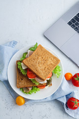Healthy sandwich with greens, ham, tomatoes and cheese in a plate next to the laptop. Lunch ideas for school or for work