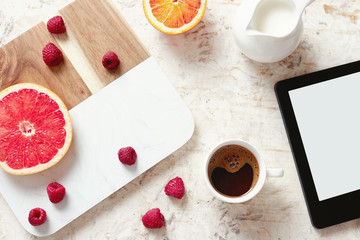 Tablet, coffee and various fresh fruits on table.