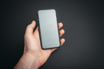 Image of mobile  held by a man hand on a dark gary background