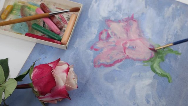 Drawing pink flower by bright pink gouache on the blue plywood on the background of pastels and pink rose