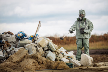 radiation supervisor in protective clothing and gas mask with geiger counter checks the level of...