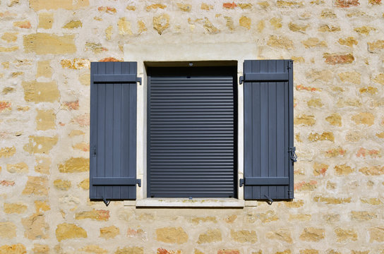 Fenêtres à volets gris sur mur de vieilles pierres