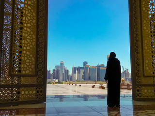 Woman with abaya dress looks at views of modern skyscrapers of Doha West Bay skyline outdoors State...