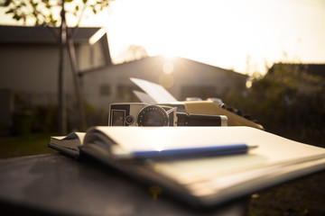 Pen and notebook, video camera and yellow typewriter on a sunny table in the back yard at sunset.