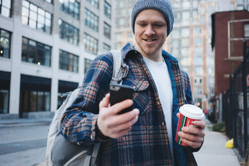 Portrait of man with cup of coffee and using mobile phone in the city