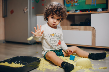 little boy playing with yellow kinetic sand on the floor at home