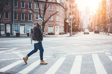 Smiling man with mobile phone walking on the city street and crossing the road