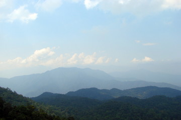 Panorama from a bird's eye view of a cloudy blue sky on the background of numerous Asian mountain ranges on a horizon covered with dense forests.