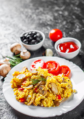 scrambled eggs with mushrooms and vegetables in white plate on dark background