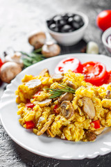 scrambled eggs with mushrooms and vegetables in white plate on dark background