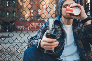 Handsome man sitting on the city street drinking cup of hot coffee and using mobile phone