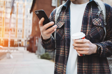 Casual man walking on the street sidewalk with cup of hot coffee and texting on telephone. Close-up