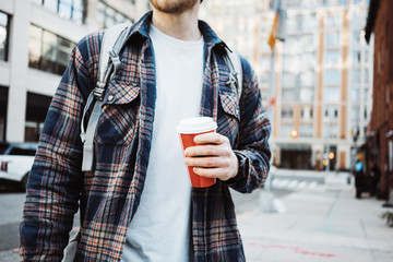 Casual man walking on the street sidewalk with cup of hot coffee. Close-up
