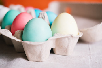Egg box with colorful Easter eggs stands on linen canvas.