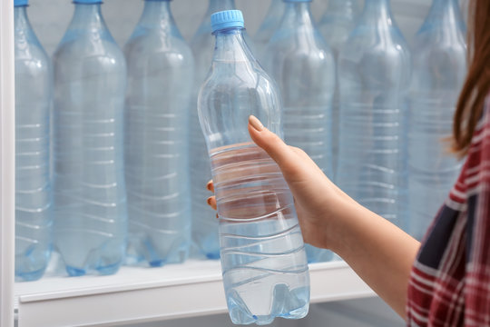 Woman Taking Bottle Of Water From Fridge In Shop