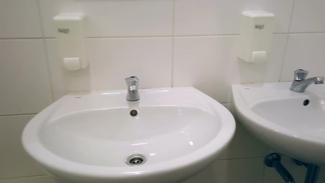 Filming womens toilet with white sinks and wall mounted soap containers. Public toilet with white ceramic tiles and separated male and female part.
