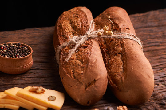Peppercorns in a wooden bowl on table with stack of bread and two baguettes. Homemade food
