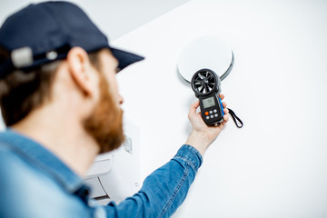 Handyman checking the speed of air ventilation with measuring tool on the white wall background