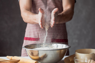 A handful of flour with egg on a rustic kitchen. Against the background of men's hands knead the dough