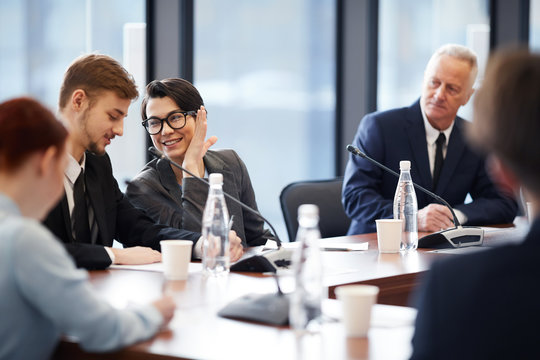 Portrait of cheerful businesswoman whispering to colleague during business meeting in conference room, copy space