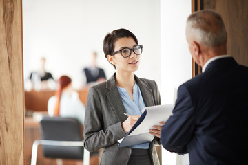 Waist up portrait of young businesswoman holding clipboard asking questions while talking to boss...