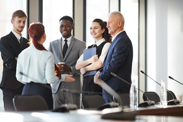 Multi-ethnic group of cheerful business people standing by window in office and communicating, copy...