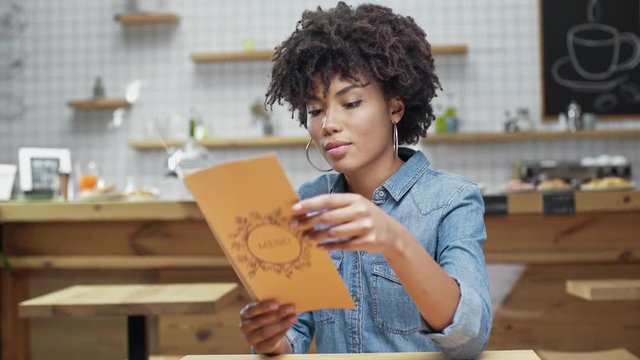 Beautiful African American Female Customer Looking At Menu And Calling For Waiter In Cafe