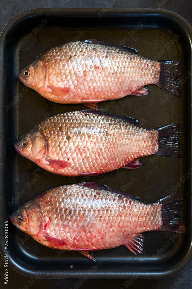 Wall mural Fresh raw carp in a pan on a black background.