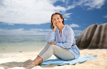 Fototapeta na wymiar people and summer concept - happy smiling woman sitting on towel over seychelles island tropical beach background