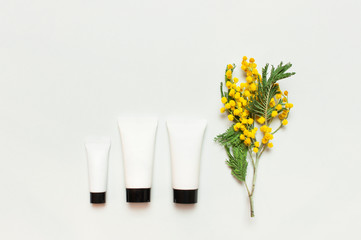 White cosmetic bottle containers with yellow Mimosa flowers on light background top view flat lay....