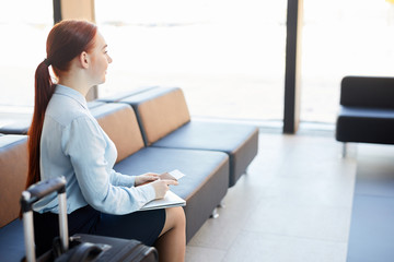 Side view portrait of young woman waiting in airport holding ticket and passport, copy space