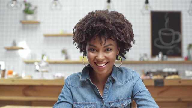 beautiful african american female customer in denim blouse looking at camera and smiling in cafe