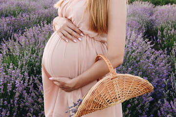 Pregnant girl blonde in a beige dress and straw hat. Lavender field. In anticipation of a child....