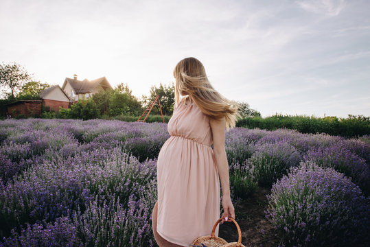 Pregnant girl blonde in a beige dress and straw hat. Lavender field. In anticipation of a child. The idea of a photo shoot. Walk at sunset. Future mom. Basket of flowers.