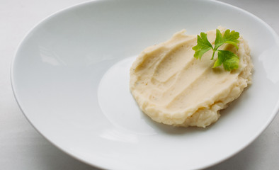 Close up of homemade dinner of mashed potatoes with parsley on white plate. Healthy and organic dish of potato cooking at home.