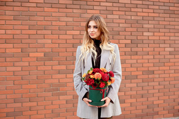 Caucasian woman standing on the street near storefront shop windows holding flower-box with happy smile
