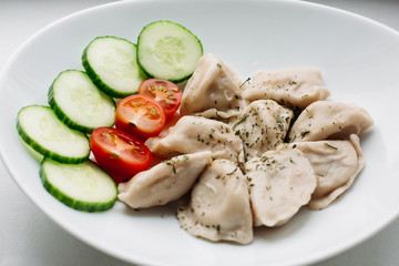 Traditional dish in Belarus, Ukraine, Russia, pirogi with different fillings, meal, potato,mushrooms, cheese. Tasty homemade food like italian ravioli with fresh vegetables cucumber and tomato.