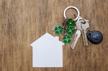 Silver keys with a keychain in the form of a four-leaf clover and a house near the wooden background