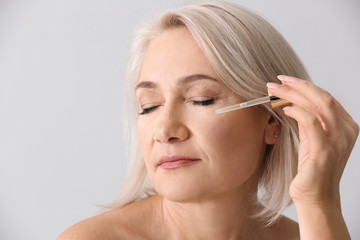 Mature woman applying face serum on light background