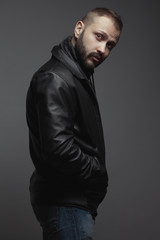 Rock star concept. Portrait of 35-year-old man standing over gray background. Modern haircut. Rocker, biker style. Hands in pockets. Street fashion. Studio shot