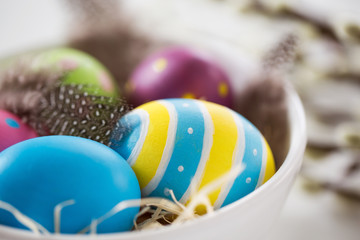 easter, holidays, tradition and object concept - close up of colored eggs and quail feathers in bowl