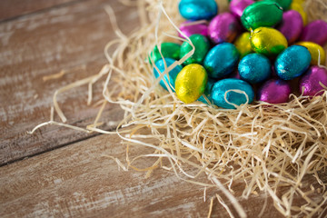 Fototapeta na wymiar easter, confectionery and holidays concept - chocolate eggs in foil wrappers in straw nest on wooden table