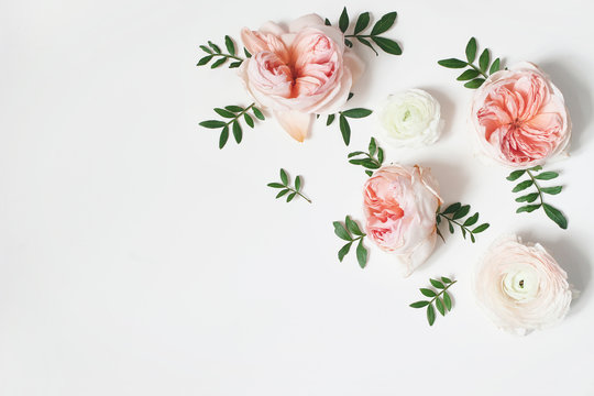 Decorative corner, floral composition with pink English roses, ranunculus and green leaves on white table background. Flower pattern. Flat lay, top view. Wedding or birthday styled stock photo.