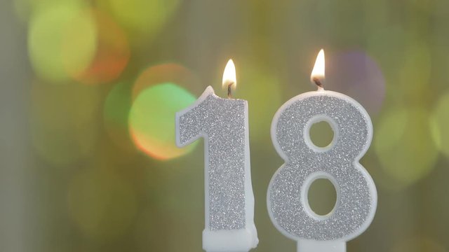 Number 18 birthday celebration candle against a bright  lights and golden bokeh background. eighteenth birthday